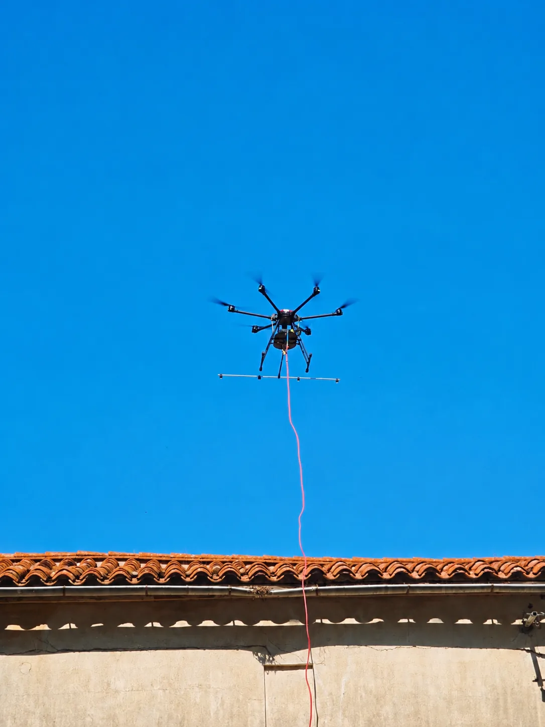 Drone hexacoptère AltiWash en vol de précision au-dessus d'une toiture en tuiles, sous un ciel dégagé